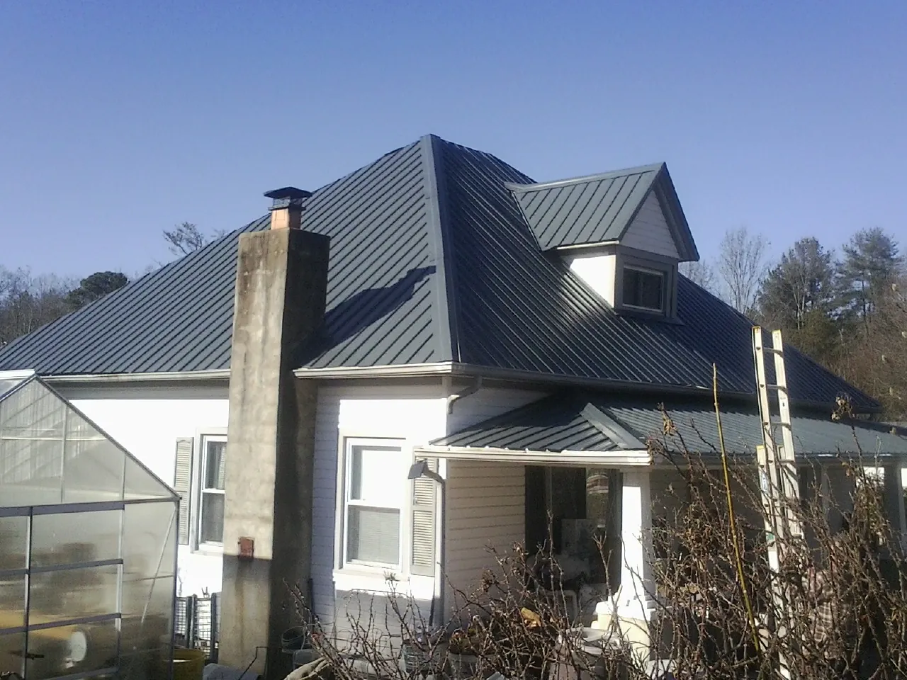 Dark blue standing seam metal roof on a white farmhouse with dormer — Slate & Tile Roof Repair by Roofing Brothers in North Springfield