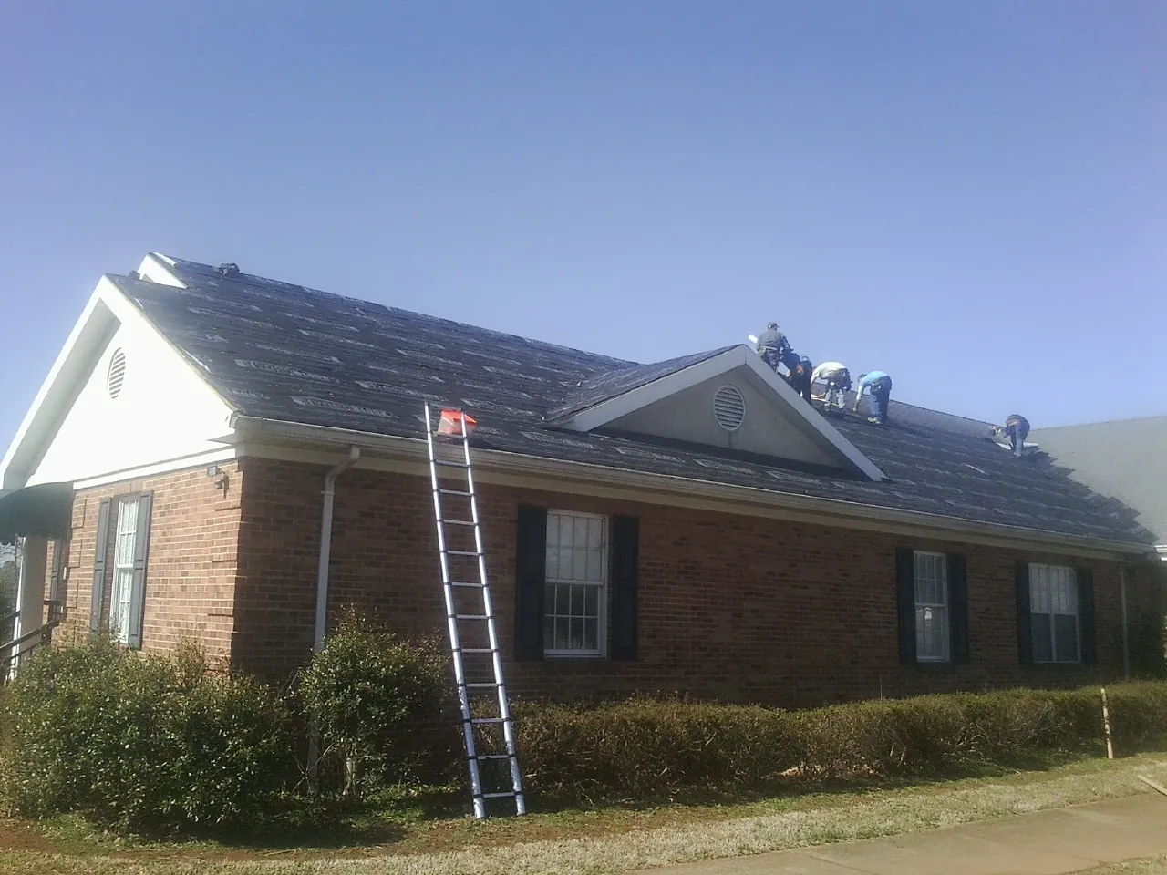 Crew tearing shingles off a brick ranch roof with a ladder set — Emergency Roof Repair work by our crew in North Springfield