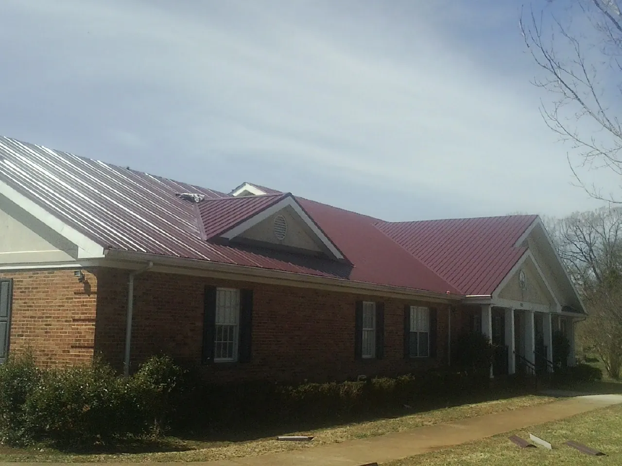 Red metal roof with gabled entries on a long brick building, from a Hail Damage Roof Repair job in North Springfield