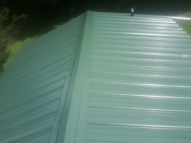 New green metal panels meeting at the ridge of a roof — Flat Roof Repair work by our crew in North Springfield