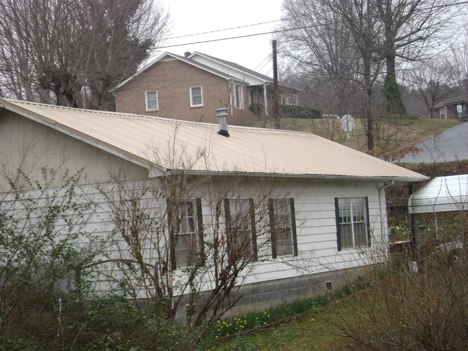 Tan metal roof on a white sided house set into a hillside — Commercial Roofing by Roofing Brothers in North Springfield